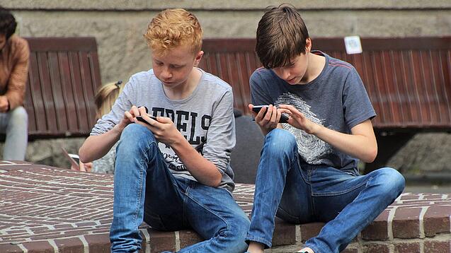 Zwei Jungs sitzen auf dem Schulhof und spielen auf ihren Smartphones.
