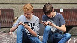 Zwei Jungs sitzen auf dem Schulhof und spielen auf ihren Smartphones.