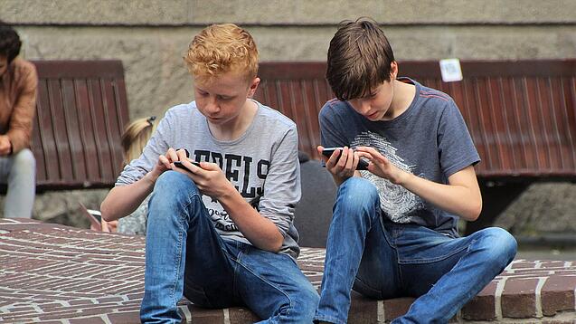 Zwei Jungs sitzen auf dem Schulhof und spielen auf ihren Smartphones.