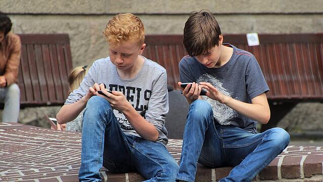 Zwei Jungs sitzen auf dem Schulhof und spielen auf ihren Smartphones.