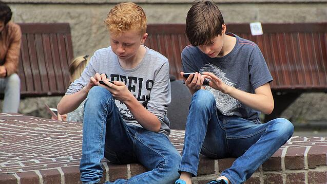 Zwei Jungs sitzen auf dem Schulhof und spielen auf ihren Smartphones.