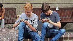 Zwei Jungs sitzen auf dem Schulhof und spielen auf ihren Smartphones.