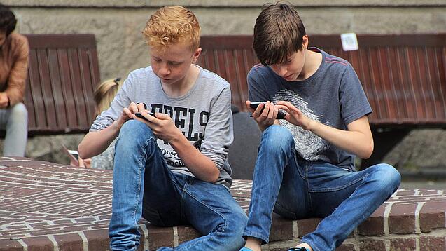 Zwei Jungs sitzen auf dem Schulhof und spielen auf ihren Smartphones.