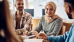 Junge Studierende sitzen an einem Gruppentisch und unterhalten sich.
