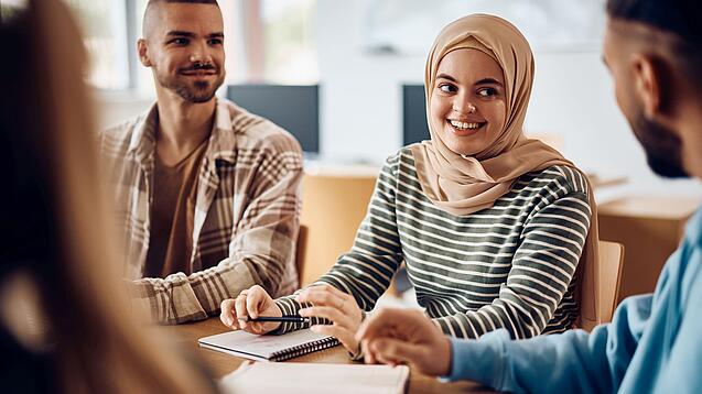 Junge Studierende sitzen an einem Gruppentisch und unterhalten sich.