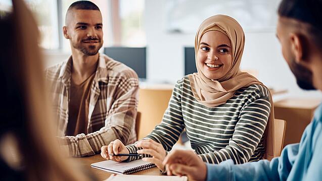 Junge Studierende sitzen an einem Gruppentisch und unterhalten sich.