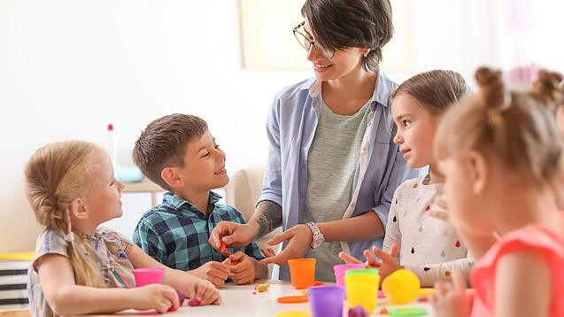 Eine Lehrerin ist mit Grundschulkindern um einen Tisch versammelt und sie bearbeiten etwas.