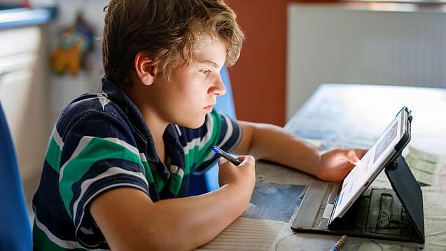 Junge sitzt vor einem Tablet und hat einen Stift in der Hand.