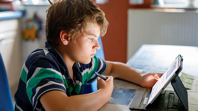 Junge sitzt vor einem Tablet und hat einen Stift in der Hand.