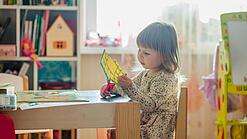 Kleines Mädchen sitzt an einem Tisch in einem Kinderzimmer und schneidet etwas aus