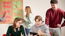 Drei Schüler:innen arbeiten an einem Tablet.
