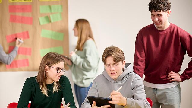 Drei Schüler:innen arbeiten an einem Tablet.