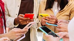Mehrere Jugendliche stehen im Kreis und schauen auf ihre Smartphones.