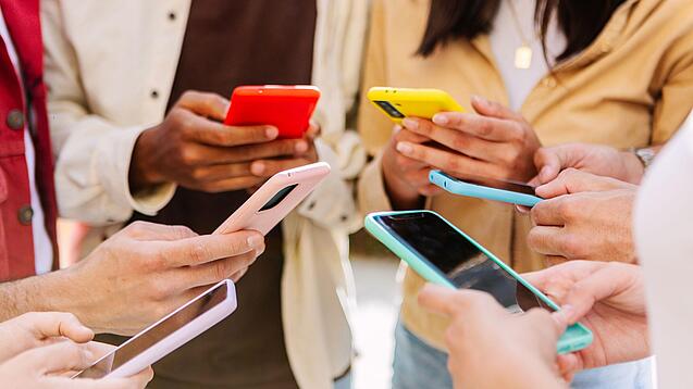 Mehrere Jugendliche stehen im Kreis und schauen auf ihre Smartphones.