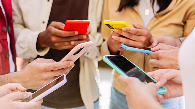 Mehrere Jugendliche stehen im Kreis und schauen auf ihre Smartphones.
