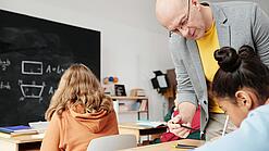 Lehrer beugt sich zu Schülerin herunter