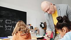 Lehrer beugt sich zu Schülerin herunter