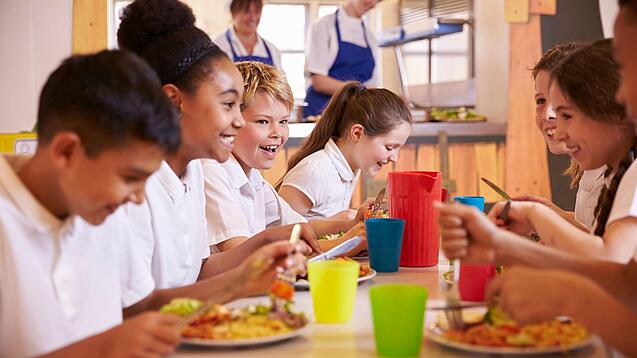 Schulkinder sitzen an einem Tisch und essen.