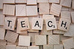 Buchstabenwürfen formen das Wort "Teach".
