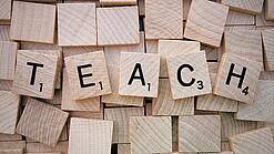 Buchstabenwürfen formen das Wort "Teach".