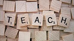 Buchstabenwürfen formen das Wort "Teach".
