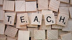 Buchstabenwürfen formen das Wort "Teach".