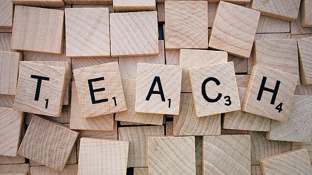 Buchstabenwürfen formen das Wort "Teach".