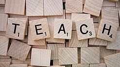 Buchstabenwürfen formen das Wort "Teach".