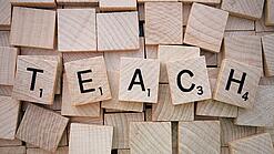 Buchstabenwürfen formen das Wort "Teach".