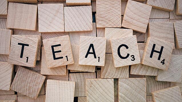Buchstabenwürfen formen das Wort "Teach".