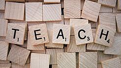 Buchstabenwürfen formen das Wort "Teach".