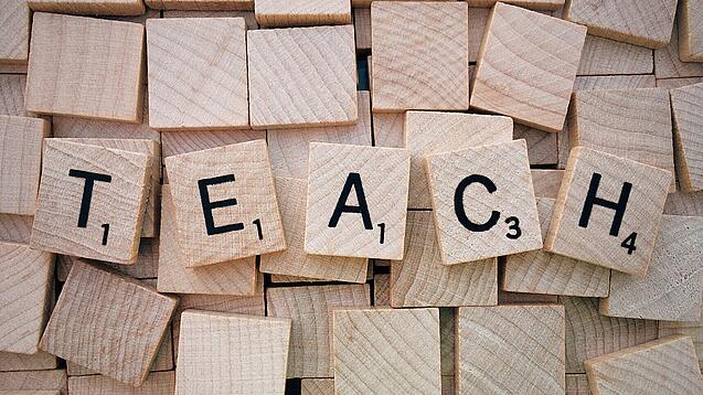 Buchstabenwürfen formen das Wort "Teach".
