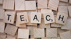 Buchstabenwürfen formen das Wort "Teach".