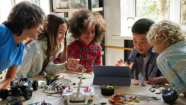 Mehrere Schülerinnen und Schüler sitzen an einem Tisch und arbeiten mit Blick auf ein Tablet.