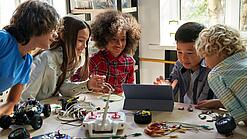 Mehrere Schülerinnen und Schüler sitzen an einem Tisch und arbeiten mit Blick auf ein Tablet.