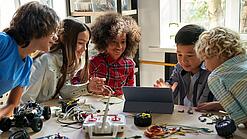 Mehrere Schülerinnen und Schüler sitzen an einem Tisch und arbeiten mit Blick auf ein Tablet.
