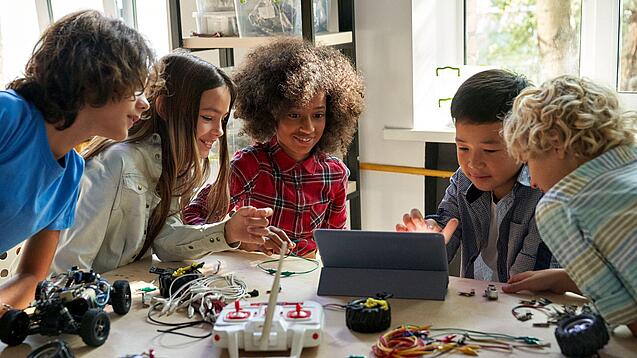 Mehrere Schülerinnen und Schüler sitzen an einem Tisch und arbeiten mit Blick auf ein Tablet.