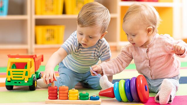 Zwei sehr kleine Kinder sitzen auf dem Boden und spielen mit Spielzeug.