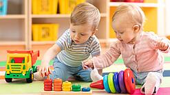 Zwei sehr kleine Kinder sitzen auf dem Boden und spielen mit Spielzeug.