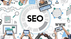 Personen sitzen an einem Tisch und nutzen Laptops, Tablets und Handys. Der Tisch zeigt einige Digitalisierungs-Symbole und den Schriftzug SEO.