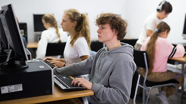 Schülerinnen und Schüler sitzen vor Computern in einem Computerraum.