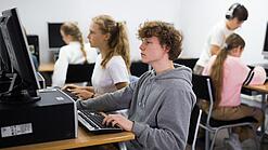Schülerinnen und Schüler sitzen vor Computern in einem Computerraum.