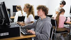 Schülerinnen und Schüler sitzen vor Computern in einem Computerraum.