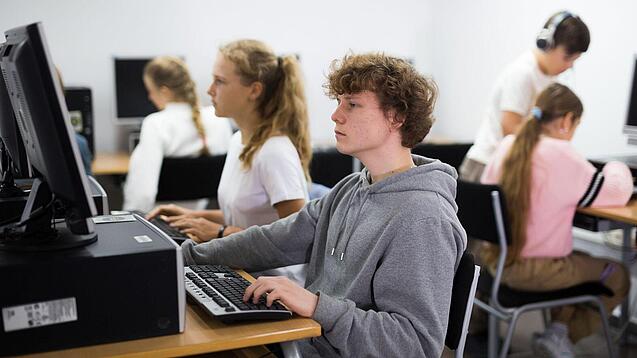 Schülerinnen und Schüler sitzen vor Computern in einem Computerraum.