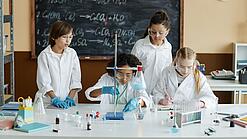 Schülerinnen und Schüler tragen weiße Kittel arbeiten an einem wissenschaftlichen Projekt.