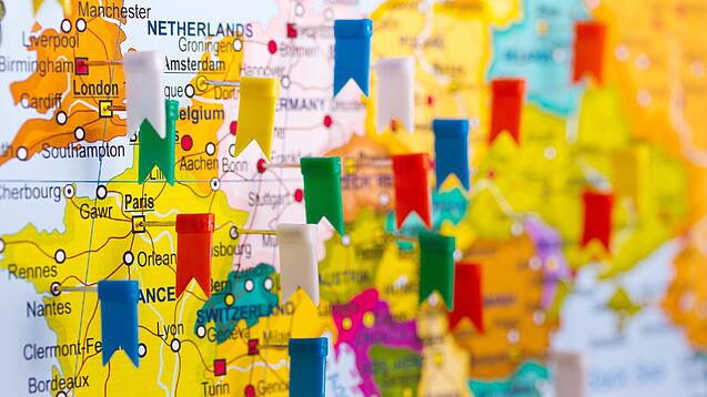 In einen Ausschnitt einer Karte von Europa sind mehrere verschiedenfarbene Fähnchen gepinnt, die verschiedene Orte symbolisieren.