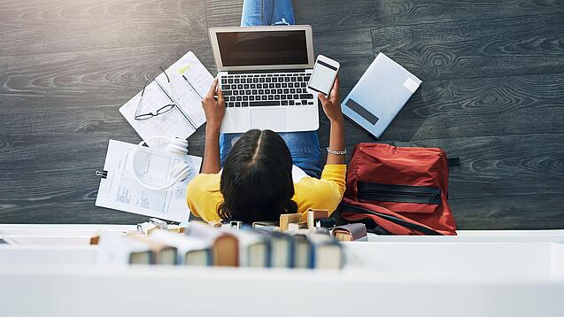 Junge Frau am Laptop vor einem Bücherregal.