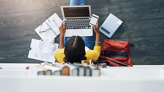 Junge Frau am Laptop vor einem Bücherregal.