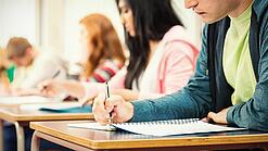 Mehrere Studierende sitzen an Tischen und arbeiten in ihren Unterlagen.