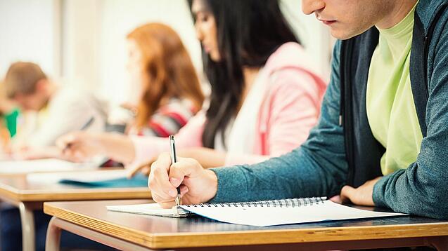 Mehrere Studierende sitzen an Tischen und arbeiten in ihren Unterlagen.